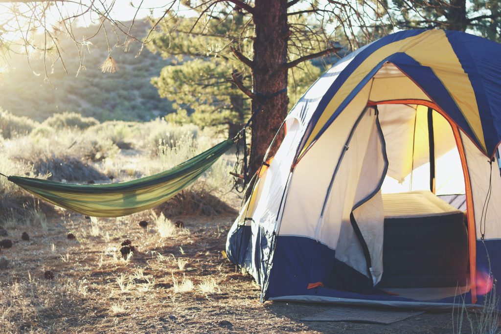 A melhor barraca de camping armada ao lado de uma rede amarrada no tronco de uma árvore.
