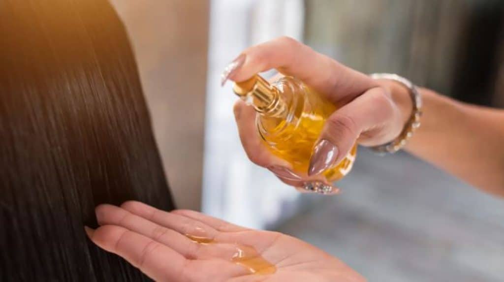 Mulher aplicando o melhor óleo capilar nas mãos próximas ao cabelo.