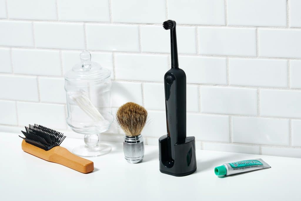 A melhor escova de dente elétrica sobre uma bancada branca e ao lado de uma escova de cabelo, escova de barbear e uma pasta de dente.