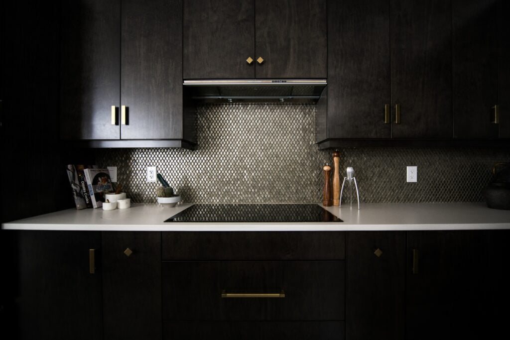 Cozinha preta com cooktop na bancada branca e o melhor depurador de ar entre os armários.