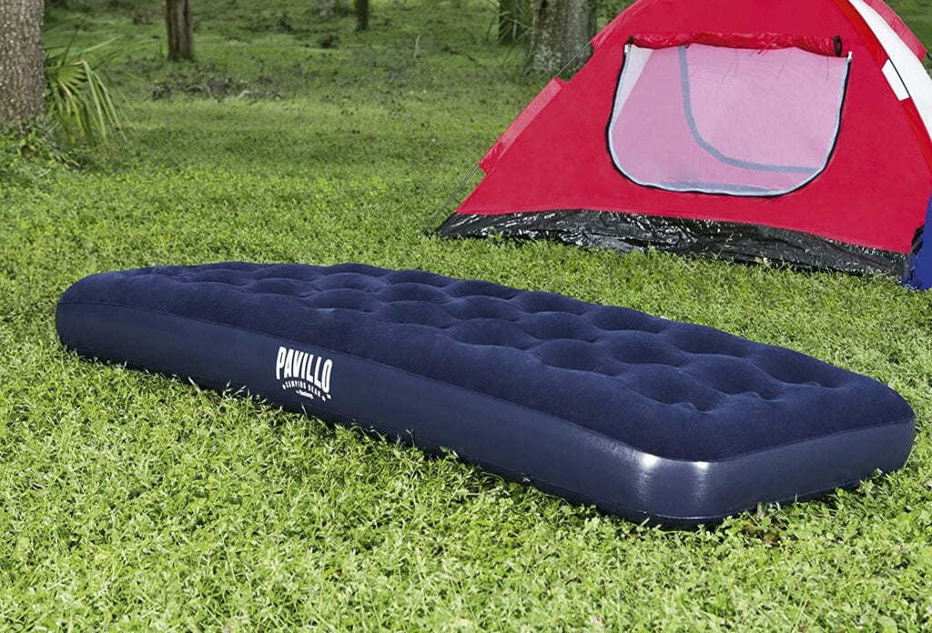 O melhor colchão inflável de solteiro em cima da grama e em frente a barraca de camping.
